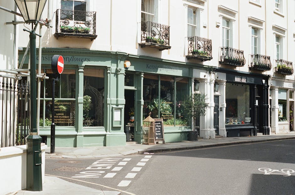 A traditional brick building housing a pub or restaurant with a deep red wooden facade, featuring large glass windows showing warm interior lighting. On the sidewalk in front, there is a black waste b